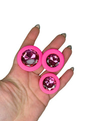 Pink circularbutt plugs with gemstone-like centers held in a hand against a white background