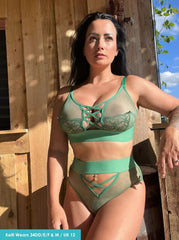 Woman wearing a green lingerie set standing outdoors near a wooden structure.