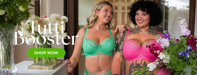Two models wearing Tutti Rouge Tutti Booster lingerie sets in mint green and bright pink pose together in an elegant floral setting. The banner showcases supportive lace bras and matching briefs, with large promotional text reading “Tutti Booster” and a “Shop Now” call-to-action.