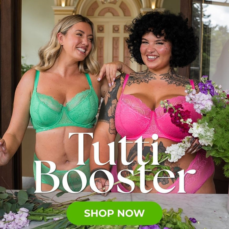 Two models wearing Tutti Rouge Tutti Booster lingerie sets in mint green and bright pink stand together indoors surrounded by fresh flowers. The image highlights supportive lace bras and matching briefs, with promotional text reading “Tutti Booster” and “Shop Now.”